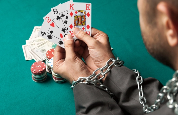 Gambler Hands Chained and Holding Cards on a Casino Table